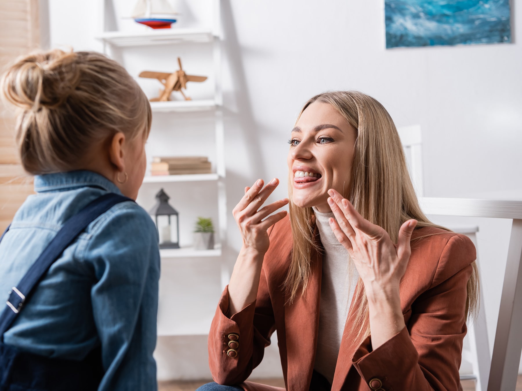 A speech language pathologist demonstrating a mouth shape to the child sitting opposite her.